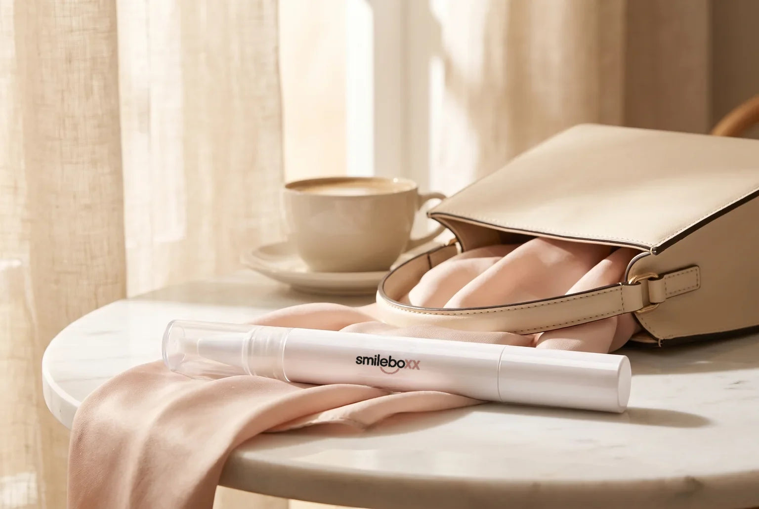 A white applicator pen printed smileboxx resting on a blush silk scarf beside an open cream handbag on a cafe table
