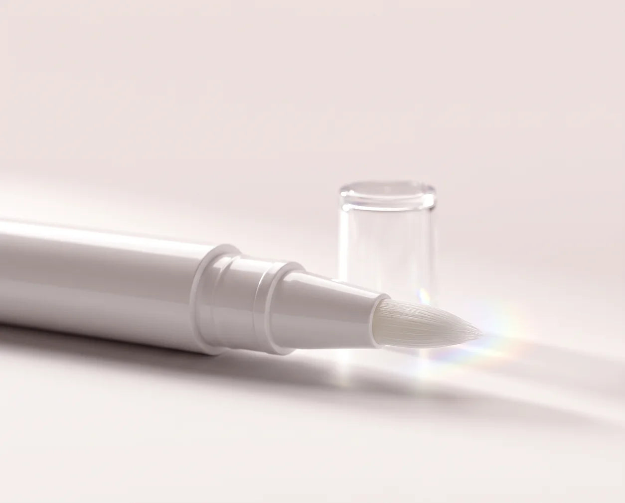 Close-up of a white applicator pen's fine brush tip beside its clear cap