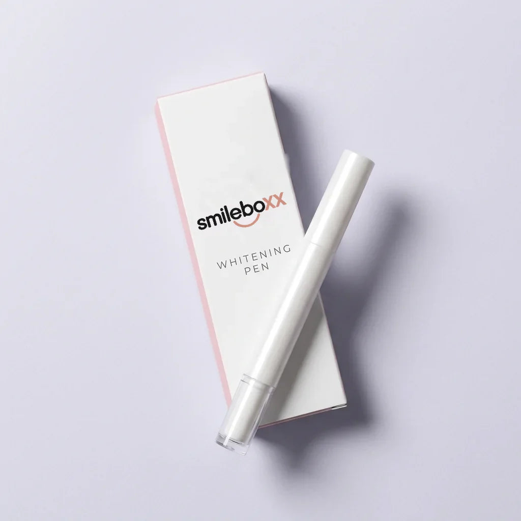 A white carton printed smileboxx and WHITENING PEN with a white applicator pen lying across it