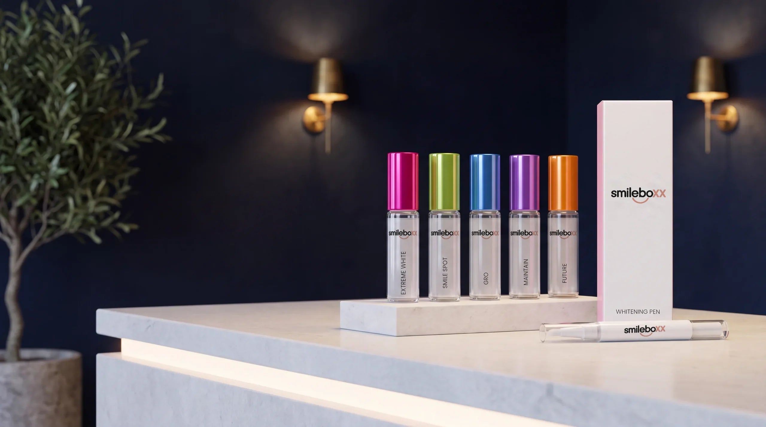 Five Smile BOXX glass ampoules on a stone riser and a carton printed smileboxx and WHITENING PEN on a pale counter in a dark studio