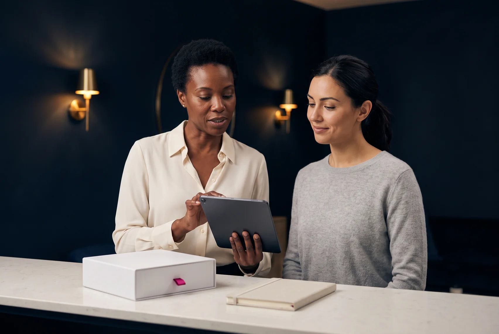 Two women reviewing a tablet together at a stone counter in a softly lit studio