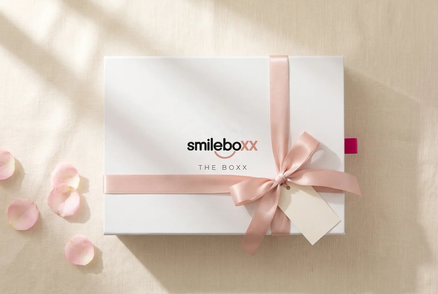 A white box printed smileboxx and THE BOXX tied with a blush satin ribbon and a blank tag