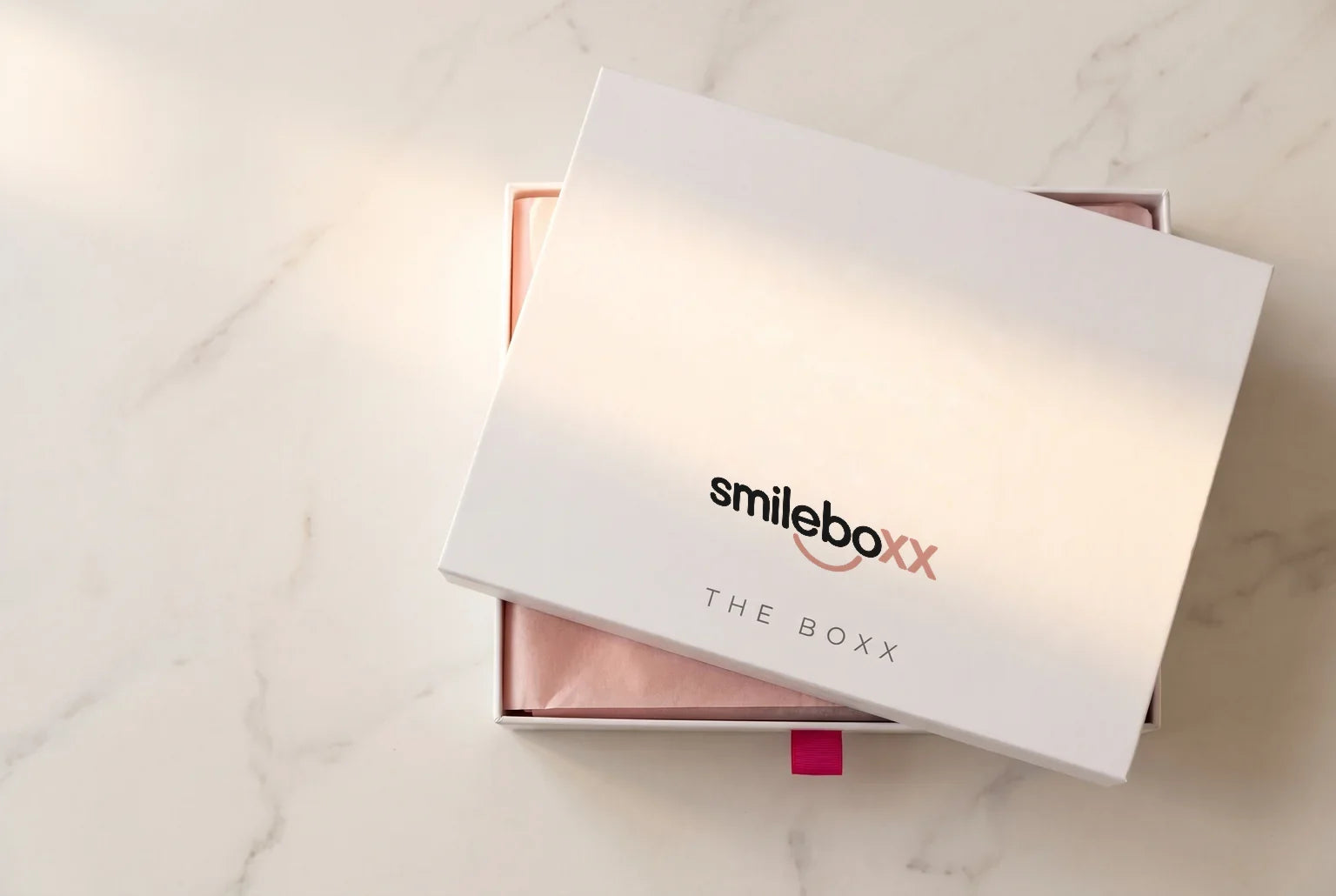 A white box printed smileboxx and THE BOXX with its lid lifted to show blush tissue paper