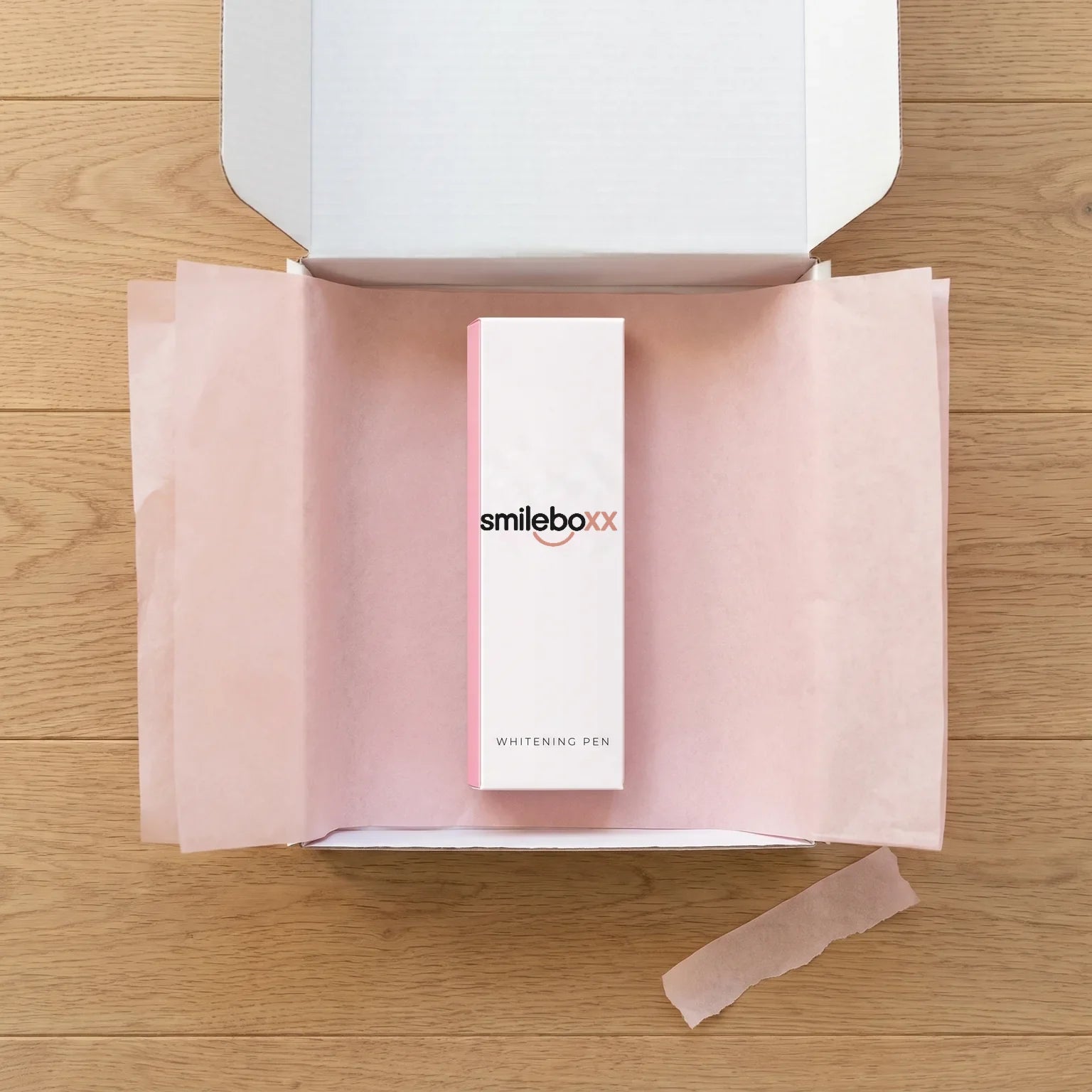 An opened white mailer box with blush tissue paper holding a carton printed smileboxx and WHITENING PEN