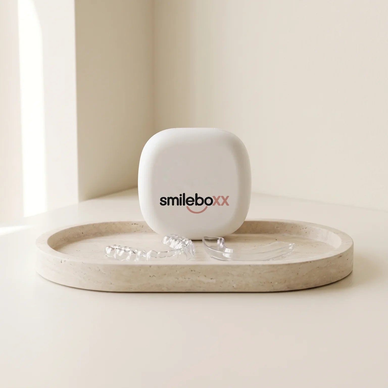 A small aligner case printed smileboxx on a stone tray with a clear aligner and a clear whitening tray