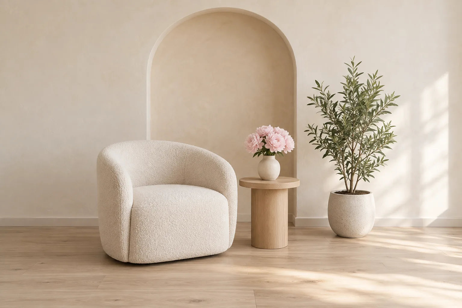 A cream armchair, a small oak side table with pink flowers and an olive tree in a softly lit arched room