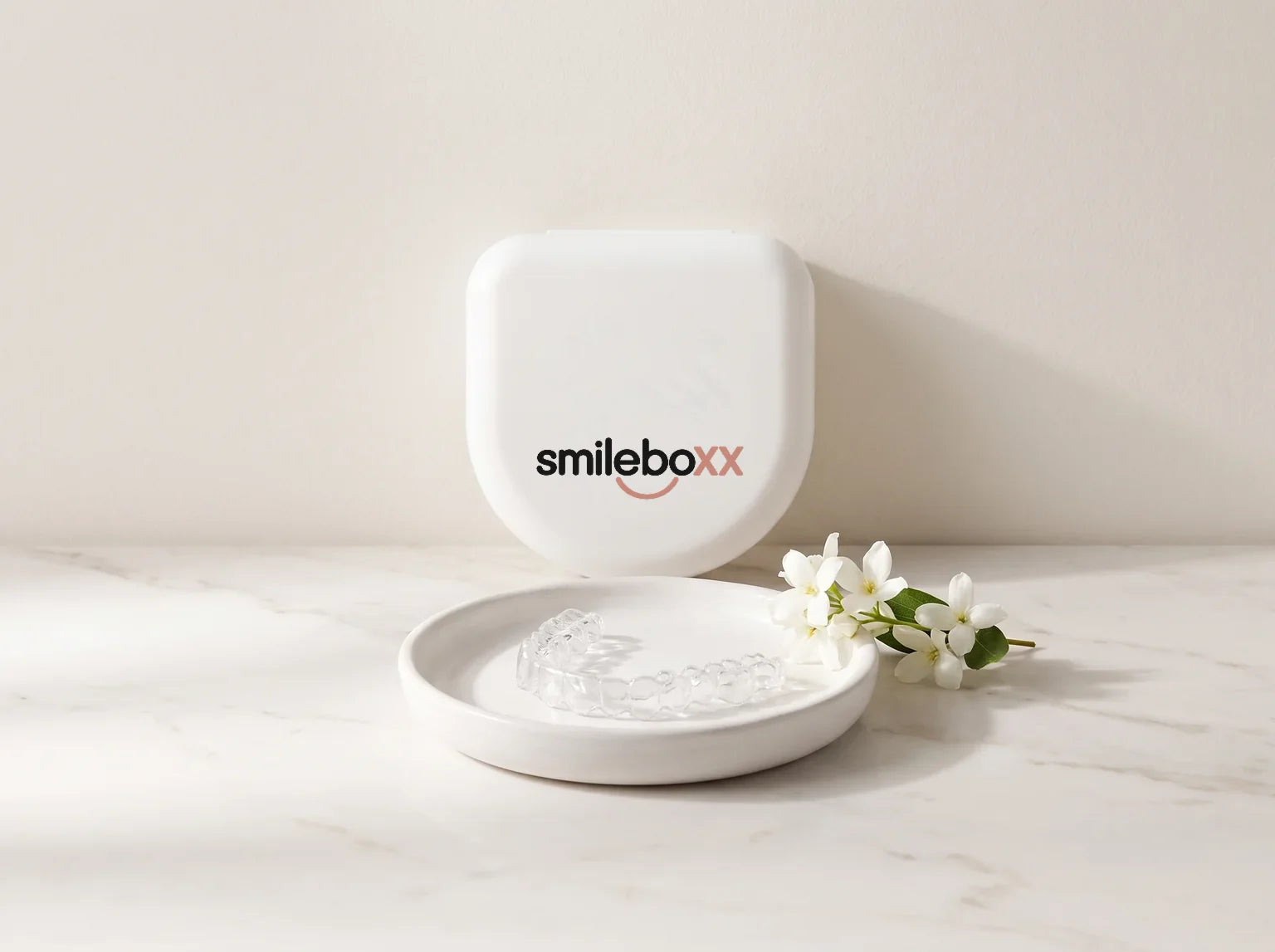 A white retainer case printed smileboxx behind a ceramic dish holding a clear retainer
